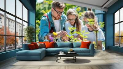 A teacher leans over two young students, pointing out details in a garden, as they take notes and observe plants Wall mural