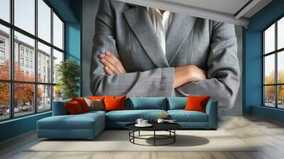 A woman in a grey suit stands with her arms crossed, confidently exuding an air of quiet strength Wall mural