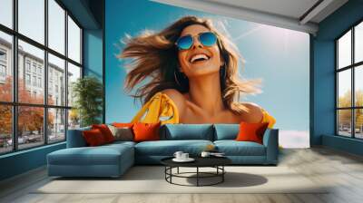 A young woman in sunglasses laughs against the background of the sky and sun Wall mural