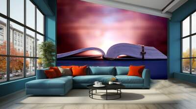 An open bible and a church cross in dark colors and a shining background. Wall mural