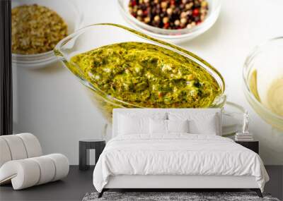 Chimichurri sauce in a gravy bowl on a white background. Various spices lie nearby. Argentinean vegetarian sauce made from olive oil, oregano, parsley. Wall mural