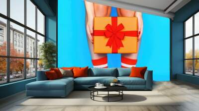 Festive Gift Box with Red Bow Held by Woman in Striped Socks on Blue Background Wall mural