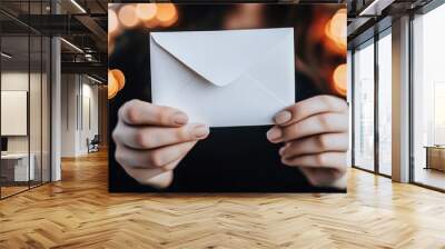 Hands holding a white envelope with warm bokeh lights in the background Wall mural