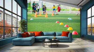 selective focus to red and yellow marker cones are soccer training equipment on green artificial turf with blurry kid players training background. material for training class of football academy. Wall mural