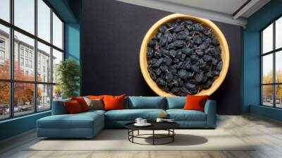 Black currant raisins in a wooden bowl on black background. Top view. Wall mural