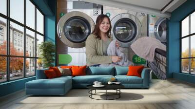 Beautiful woman enjoying clean clothes in the self service laundry with dryer machines on the background Wall mural