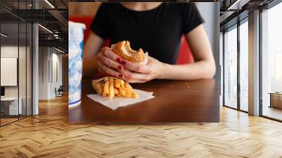 Young girl holding in female hands fast food burger, american unhealthy meal on blue background, mockup with copy space for text message or design, hungry human with grilled hamburger front view Wall mural