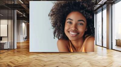  A beautiful mixed race model with curly hair, smiling and posing in front of the camera wearing a denim vest top, hands behind her head against a white background Wall mural