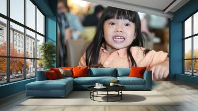 Asian children cute or kid girl enjoy and fun with happy eating delicious brownie chocolate cake for sweet dessert or snack on wood table and smile white teeth at lunch in restaurant or cafe Wall mural