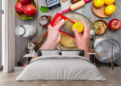 hands of a cook woman rub the zest of a lemon for making a pie. Top view of kitchen table, dough and sweet dessert ingredients. Wall mural