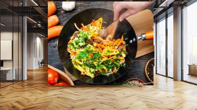 woman's hands stir hot vegetables and meat in a wok. Top view, close-up. Wall mural