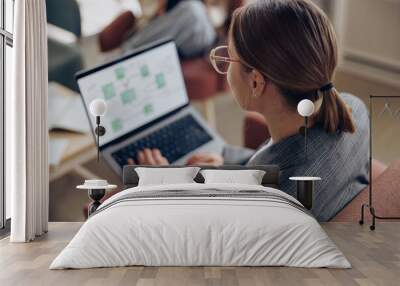 Back view of female freelancer working on laptop while sitting in modern coworking  Wall mural