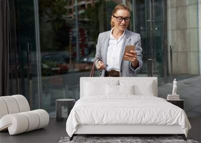 Checking important email. Portrait of a confident attractive business woman in classic wear using smartphone on the way to office Wall mural