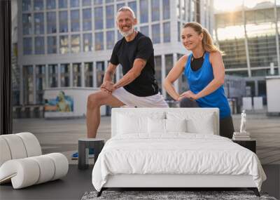 Cheerful sporty middle aged couple, man and woman warming up, getting ready for running together in the city on a summer day Wall mural