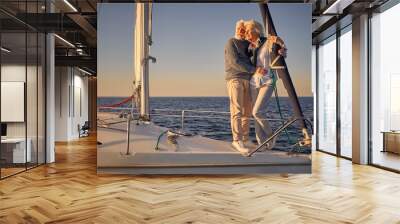 Full length of beautiful romantic senior couple standing on the side of sail boat or yacht deck floating in the calm blue sea, hugging and enjoying amazing sunset Wall mural