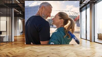 Lovely sportive middle aged couple smiling at each other while standing together outdoors, ready for morning workout on tennis court Wall mural