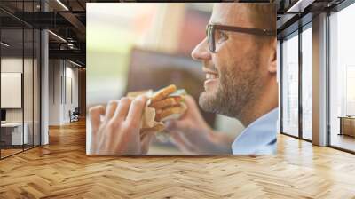 Lunch time. Close up shot of happy young man eating sandwich while working remotely in cafe, taking a break Wall mural