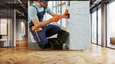 Male electrician fixing electrical wall socket with screwdriver Wall mural