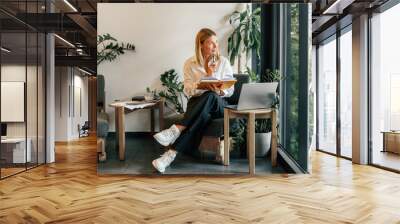 Mature business woman working on laptop, making notes in cozy coworkign space interior Wall mural