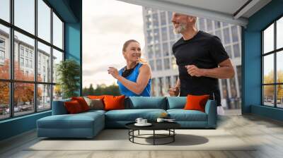 Portrait of active middle aged couple, man and woman in sportswear looking happy while jogging together outdoors, having mroning workout Wall mural