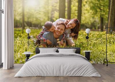 Portrait of happy Caucasian family lying in hugs on green grass in park on sunny summer day. Wall mural