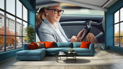 Side view of happy beautiful business woman sitting on back seat in the car and working online, she is digital tablet Wall mural