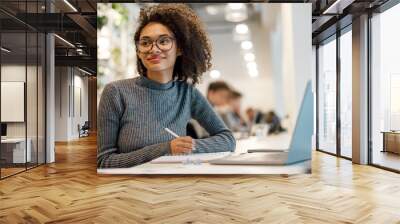 Smiling afro american woman student studying online while sitting in cozy cafe Wall mural