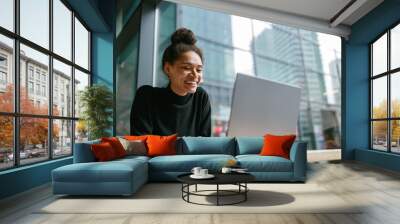 Smiling female freelancer working on laptop while sitting in cafe near window. Distance work  Wall mural