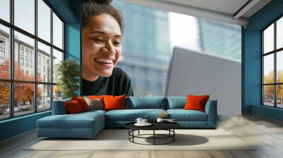 Smiling female freelancer working on laptop while sitting in cafe near window. Distance work Wall mural