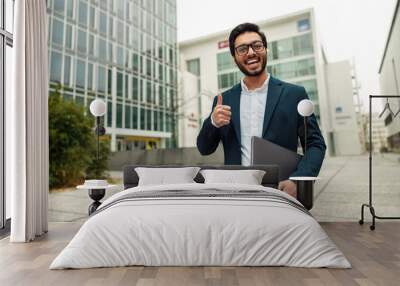 Smiling indian businessman in suit and glasses with laptop near office building Wall mural