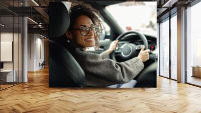 Smiling woman manager driving car and holding both hands on steering wheel on the way to work Wall mural