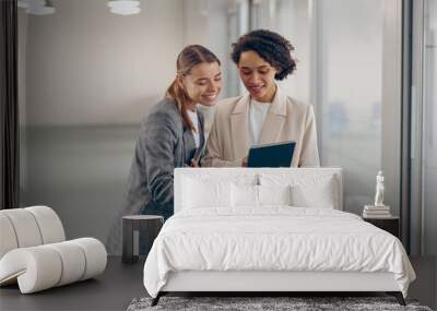 Stylish busy female coworkers discussing project standing in modern office and use digital tablet Wall mural