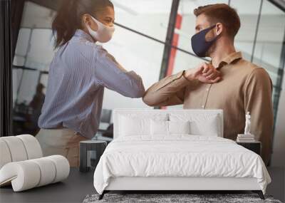 Two young diverse business colleagues wearing face protective masks bumping elbows, greeting each other while working during covid 19 quarantine Wall mural