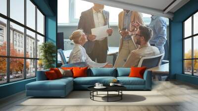 Vertical shot of cheerful multiracial business people having a meeting in the modern office, discussing work and smiling Wall mural