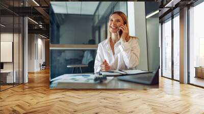 Woman sales manager talking by phone with client sitting in modern coworking and working on laptop Wall mural