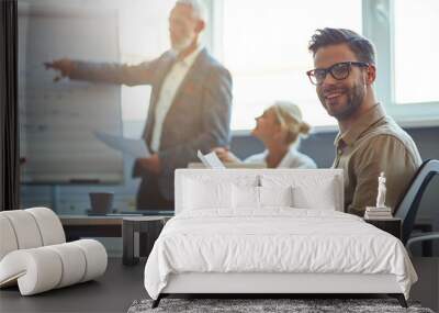 Young cheerful male office worker smiling at camera while having a meeting with collegues in the modern office Wall mural