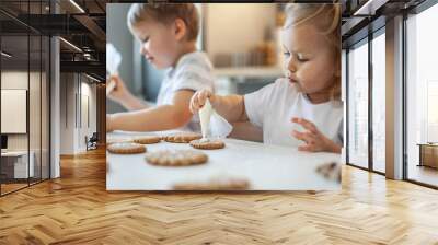 children decorate Christmas gingerbread at home. A boy and a girl paint with cornets with sugar icing on cookies. New Year's decor, branches of a Christmas tree. Wall mural