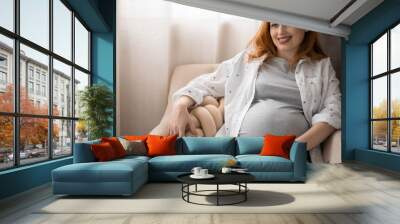 Happy young redhead pregnant woman lying on comfortable armchair Wall mural