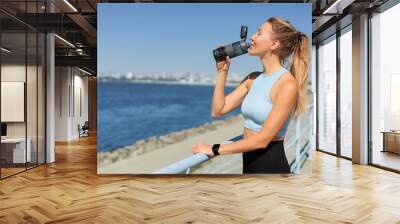 Sport woman jogger runner drinking water from bottle at city embankment river closeup Wall mural