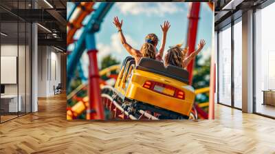 Two women riding roller coaster at theme park with their arms in the air. Wall mural