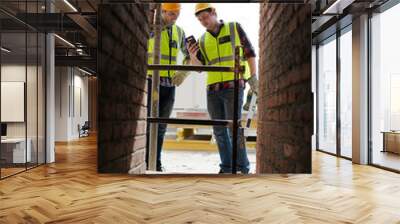 Construction workers texting with cell phone at construction site Wall mural