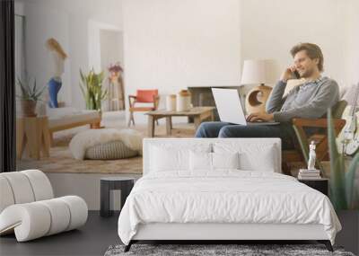 Man talking on cell phone and using laptop in living room Wall mural