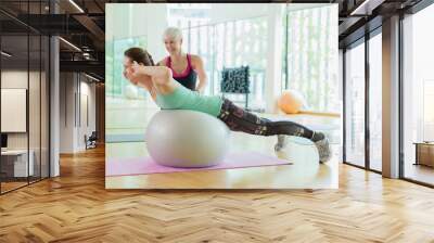 Personal trainer guiding woman doing back extensions on fitness ball  Wall mural