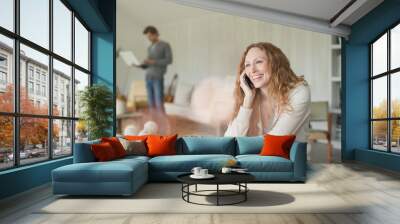 Smiling woman talking on cell phone at dining table Wall mural