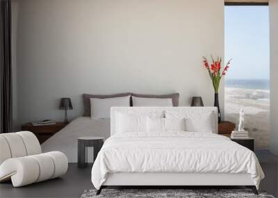 Vase of flowers next to bed in bedroom with ocean view Wall mural