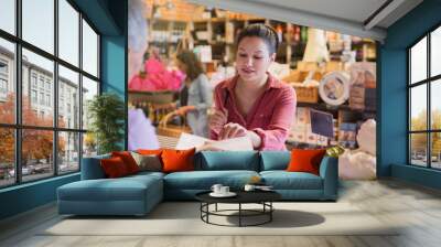 Woman sampling cheese at deli counter in market Wall mural