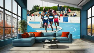 Three female endurance runners race on a blue track. Track and field illustration photo. Sports and motivational photo for movement and a healthy lifestyle Wall mural