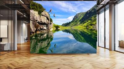 Young couple jump together into lake in mountains with beautiful blue water and reflexion. Wall mural