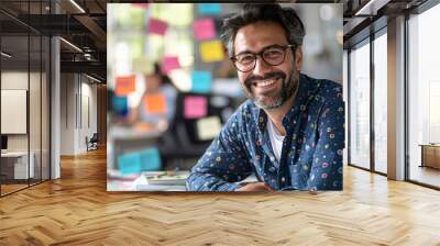 a cheerful professional man working at his desk, with a laptop open in front of him and papers scattered around, a bright office environment with sticky notes on the glass partition in the background. Wall mural