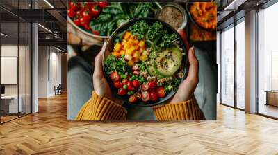 A person is holding a bowl of food that contains a variety of vegetables and fruits. The bowl is placed on a table, and there are other bowls and plates of food around it Wall mural